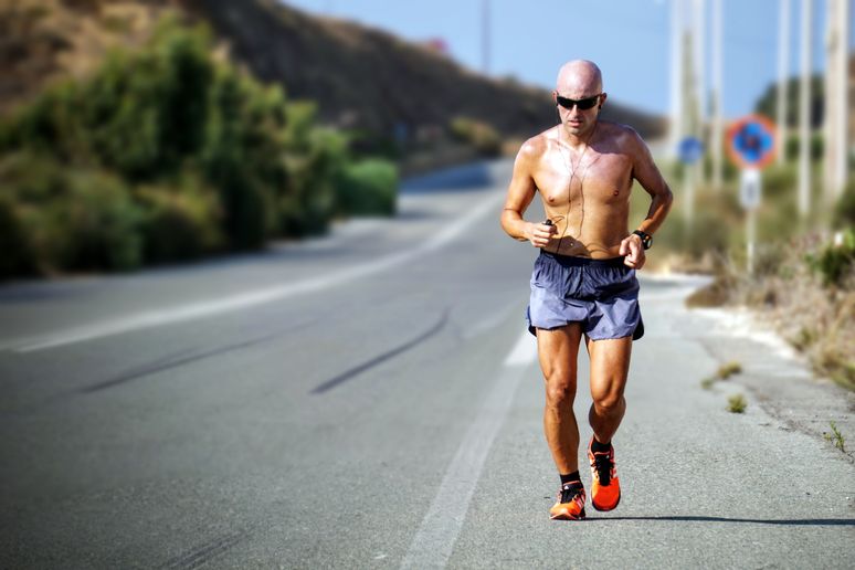 Shirtless bald man jogging along road using mobile fitness health app