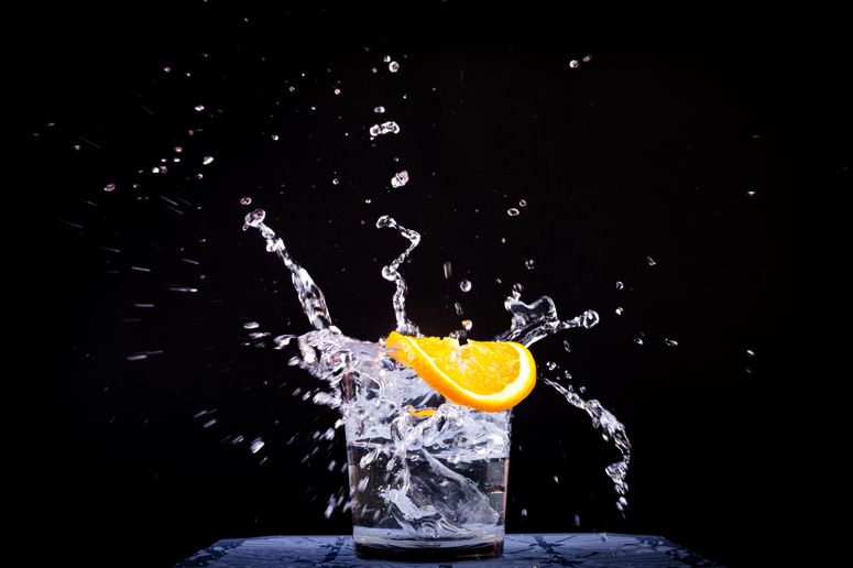 An orange slice being dropped into a glass of water
