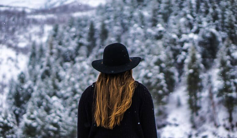 Woman wearing black winter clothing who might have seasonal depression looks at snow-covered forest in distance